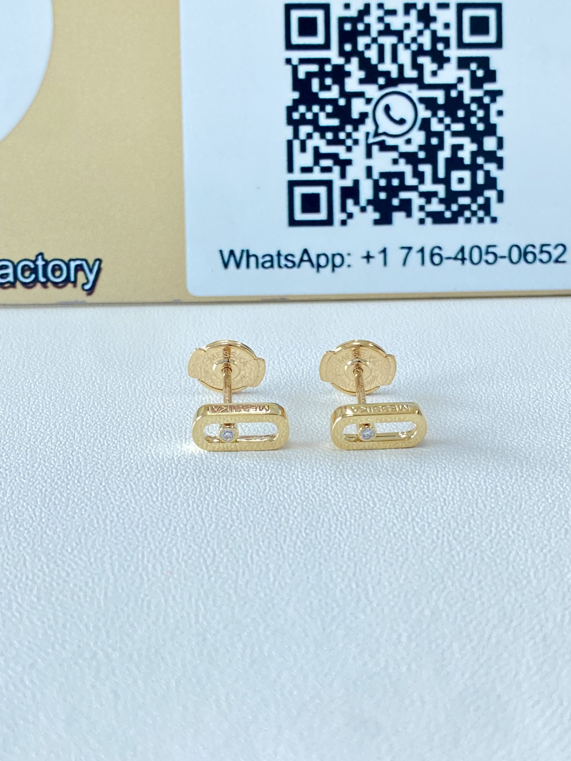 Pair of yellow gold Move Uno style stud earrings displayed in front of a QR code sign